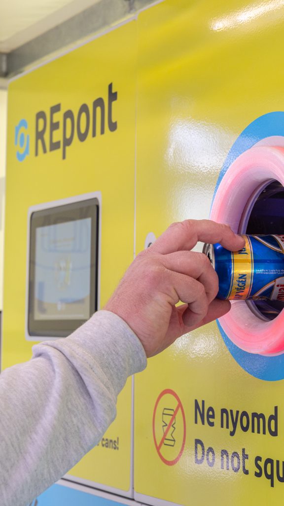 User returning an aluminum can into a festival mobile reverse vending machine with illuminated return opening and touchscreen interface